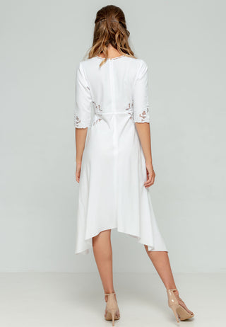 Elegant V-neck knee length white dress in rayon having asymmetric hemline and 3/4th sleeve length, with exhaustive Balinese handmade lacework on sleeves and sides of waist and pleats to contour the waistline.