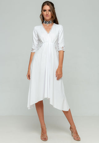 Elegant V-neck knee length white dress in rayon having asymmetric hemline and 3/4th sleeve length, with exhaustive Balinese handmade lacework on sleeves and sides of waist and pleats to contour the waistline.
